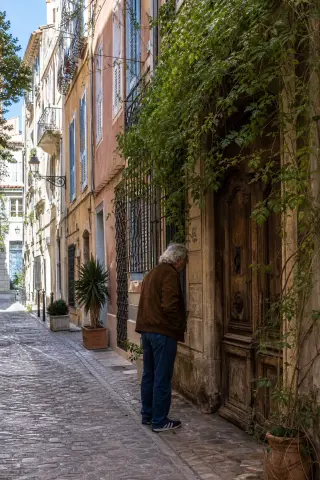 Local artist sketching quietly in a shaded courtyard near old stone buildings and leafy vines, soft afternoon light creating a tranquil, Mediterranean mood.